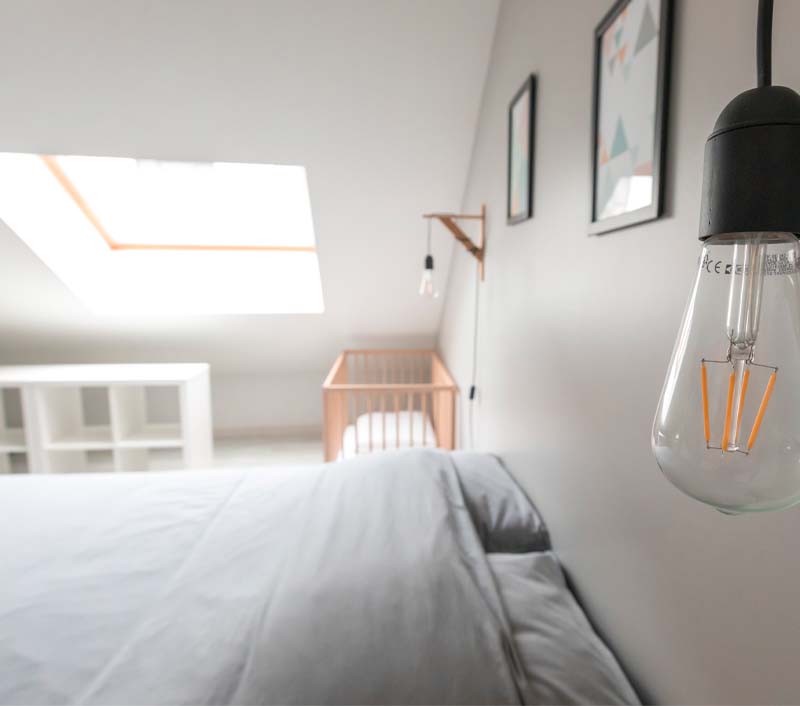 Chambre lit double ambiance scandinave. Linge de lit gris clair, bois clair, lampe de chevet, meuble blanc. Aménagement décoration intérieur Amiens